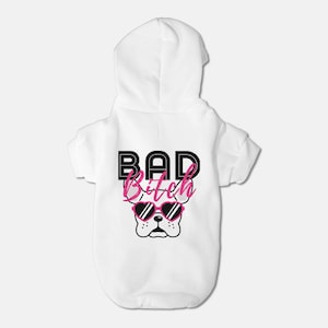 Puede incluir: Mono blanco con capucha y mangas cortas para una mascota. El mono tiene un gráfico en blanco y negro de un perro con gafas de sol de corazón rosa y el texto "BAD Bitch".