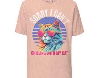 Könnte beinhalten: Pfirsichfarbenes T-Shirt mit einer Grafik einer Katze mit rosa Sonnenbrille, vor einem blau-violett gestreiften Hintergrund. Der Text "SORRY I CAN'T" wölbt sich über der Katze, darunter "CHILLING WITH MY CAT".