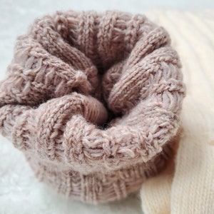 Pode incluir: Um close-up de um tecido de malha macio e rosa com um padr&atilde;o de malha de cabo. O tecido est&aacute; dobrado sobre si mesmo, criando uma forma circular.