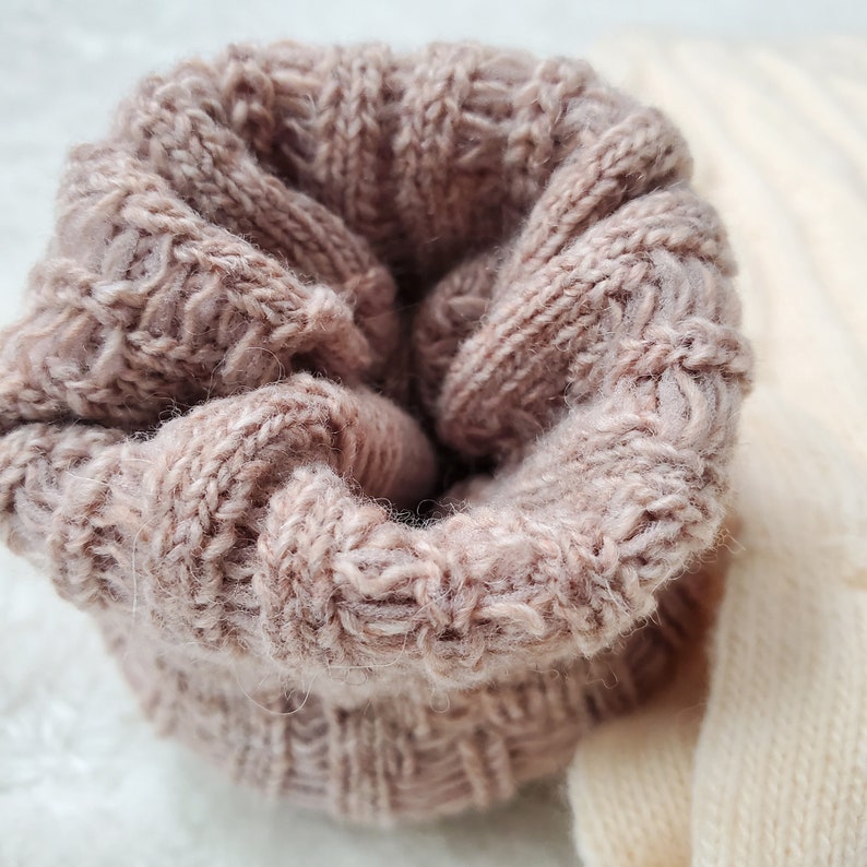 Pode incluir: Um close-up de um tecido de malha macio e rosa com um padr&atilde;o de malha de cabo. O tecido est&aacute; dobrado sobre si mesmo, criando uma forma circular.
