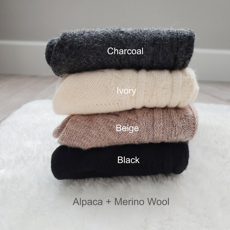 Pode incluir: Uma pilha de quatro su&eacute;teres de alpaca e l&atilde; merino em diferentes cores: carv&atilde;o, marfim, bege e preto. Os su&eacute;teres est&atilde;o dobrados e empilhados um em cima do outro. O texto "Alpaca + Merino Wool" est&aacute; impresso abaixo da pilha de su&eacute;teres.
