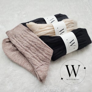 Pode incluir: Tr&ecirc;s pares de meias em bege, preto e branco com um padr&atilde;o de tric&ocirc; tran&ccedil;ado. Cada par tem uma etiqueta branca com um "W" preto e a palavra "WINTERING" nela.