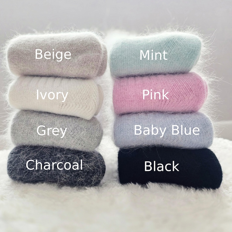 May include: Two stacks of fuzzy socks in various colours. The left stack includes beige, ivory, grey, and charcoal socks. The right stack includes mint, pink, baby blue, and black socks. Each pair is labelled with its corresponding colour name.