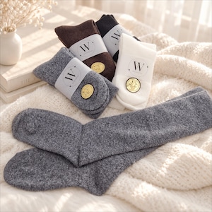 May include: A collection of knit socks in charcoal gray, brown, black, and white. Each pair is folded and secured with a white paper band featuring the letter W and the text WISTERING, accompanied by a small circular gold-toned emblem.