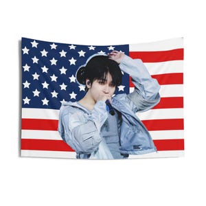 May include: A person wearing a light blue jacket with a microphone in their hand, standing in front of an American flag.