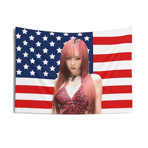 Puede incluir: Un tapiz con la bandera estadounidense como telón de fondo. Frente a la bandera hay una persona con cabello rosado y un top rojo con estampado de leopardo. La persona lleva un collar negro.