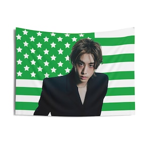 Könnte beinhalten: Eine Wandbehang mit dem Porträt einer Person mit dunklen Haaren und einem schwarzen Blazer vor dem Hintergrund einer amerikanischen Flagge mit grünen und weißen Streifen.