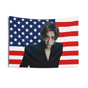 Könnte beinhalten: Eine Person mit dunklen Haaren trägt einen schwarzen Blazer und steht vor einer amerikanischen Flagge. Die Flagge ist rot, weiß und blau mit Sternen in der oberen linken Ecke.