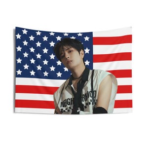 May include: A young man with black hair and a nose ring is wearing a white sleeveless shirt with a black and white checkered pattern that says "Neighborhood". He is standing in front of an American flag.