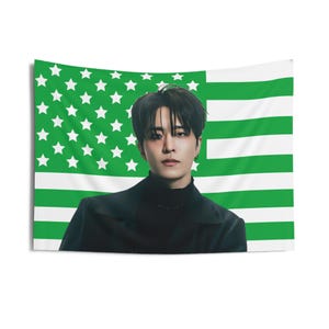 Könnte beinhalten: Eine schwarz-grüne amerikanische Flagge mit einem darübergelegten Männergesicht. Der Mann trägt ein schwarzes Hemd mit Stehkragen und eine schwarze Jacke.