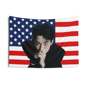 Könnte beinhalten: Eine schwarz-weiße Wandbehänge mit einem Porträt einer Person mit schwarzen Haaren und einem schwarzen Hemd vor dem Hintergrund einer amerikanischen Flagge.