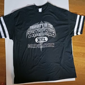 May include: Black t-shirt with white stripes on the sleeves. The shirt has a graphic print of a bat-like logo with the text "Property of the Triyche Corporation" and "XXL" in white.
