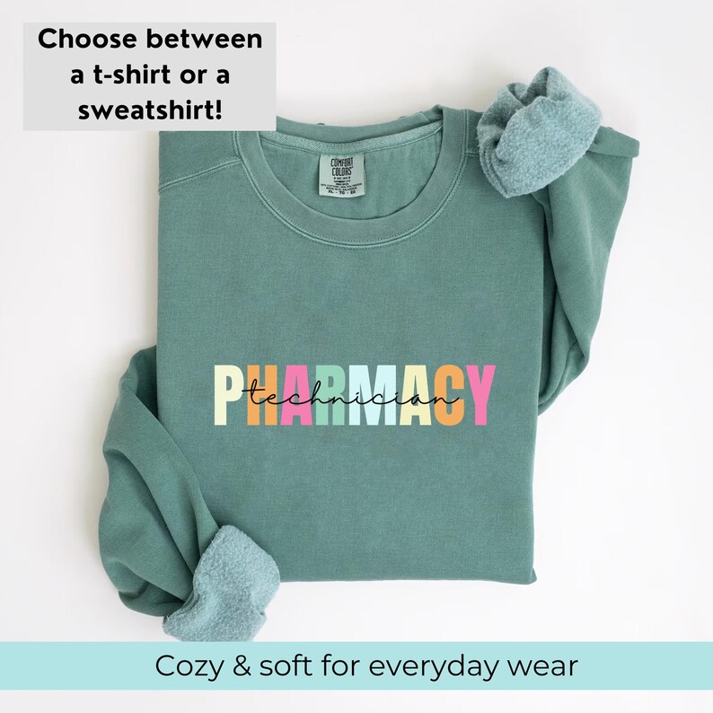May include: A teal green sweatshirt with the text "PHARMACY technician" in rainbow colours. The sweatshirt is folded and displayed on a white background.