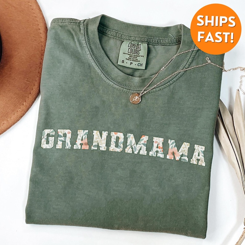 以下が含まれることがあります： 花柄の白い文字で「GRANDMAMA」と書かれた緑色のTシャツ。