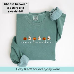 May include: Teal blue sweatshirt with a white graphic of ghosts carrying pumpkins and the text "social worker".
