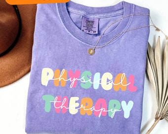 Op de afbeelding: Paars T-shirt met de woorden "PHYSICAL THERAPY" in kleurrijke bubbelletters.