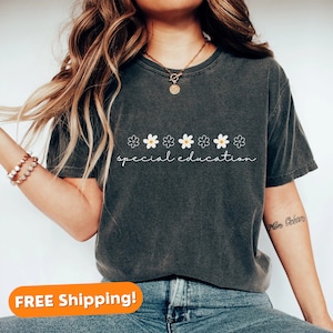 May include: A dark grey t-shirt with a row of white daisies and the text "special education" printed on the front. The shirt is being worn by a person with long brown hair.