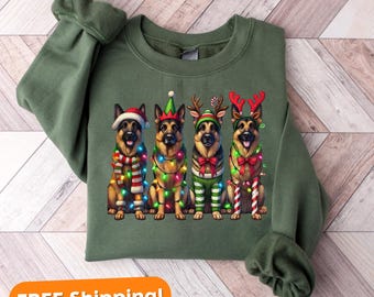 May include: A green sweatshirt with a Christmas-themed design featuring four German Shepherd dogs dressed in festive attire. The dogs are wearing Santa hats, elf hats, reindeer antlers, and candy cane accessories. They are surrounded by Christmas lights.