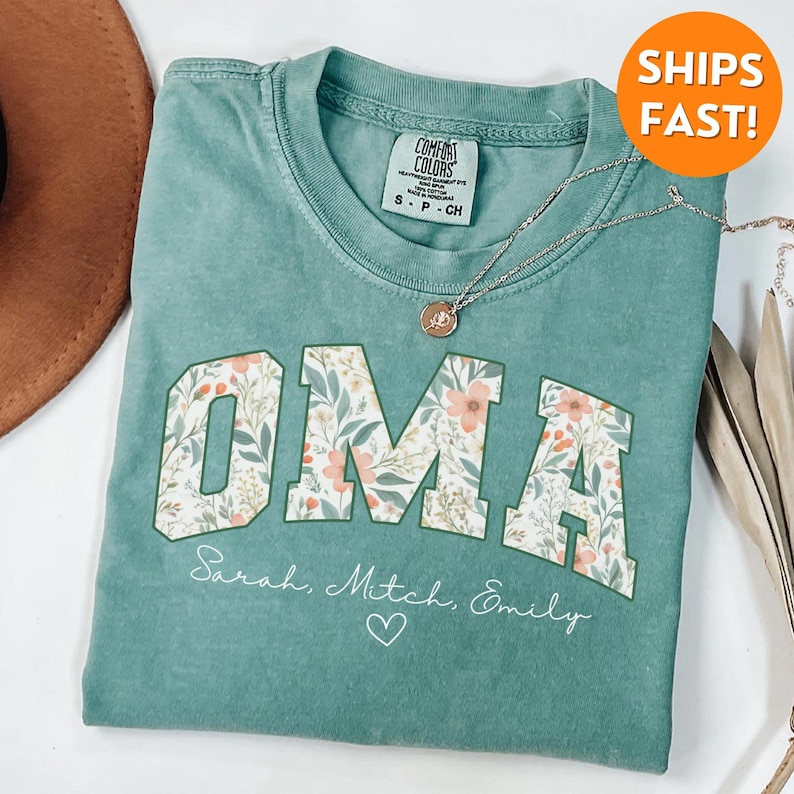 May include: A teal blue t-shirt with a white floral print that says "OMA" with the names "Sarah, Mitch, Emily" and a heart underneath.