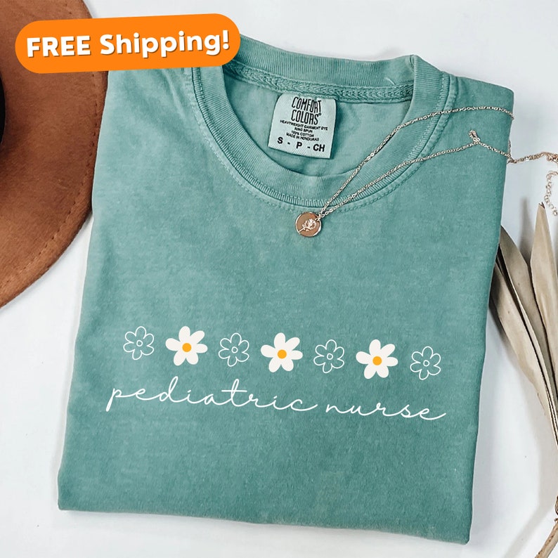 May include: A teal blue t-shirt with a row of white daisies and the text "pediatric nurse" in white.