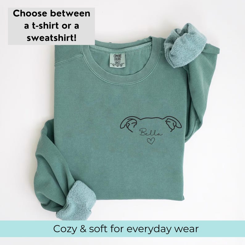 Pode incluir: Uma camisa de moletom verde-azulada com um desenho de linha preta de uma cabe&ccedil;a de cachorro com o nome "Bella" e um cora&ccedil;&atilde;o embaixo.