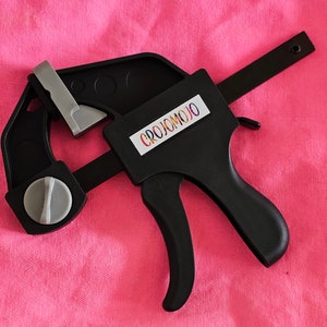 May include: Black clamp with a silver handle and a white label that says "CROJOMOJO".
