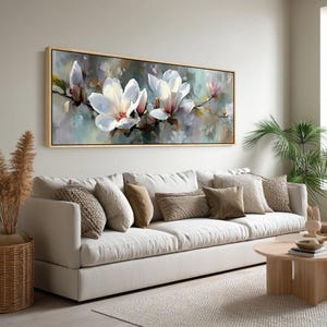 Peut inclure: Peinture rectangulaire encadrée de fleurs de magnolia blanches avec des centres roses. L'œuvre d'art est placée sur un fond abstrait doux de bleus, de verts et de violets. Le tableau est accroché au-dessus d'un canapé blanc avec divers coussins aux tons neutres.