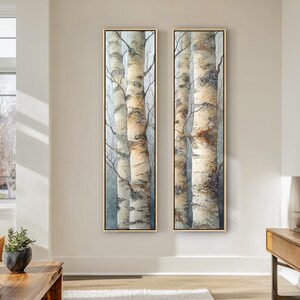 May include: Two framed vertical art pieces depict birch trees in a misty forest. The artwork features the white and brown bark of the trees, with delicate branches reaching upwards. The frames are a light brown color, and the overall aesthetic is serene.
