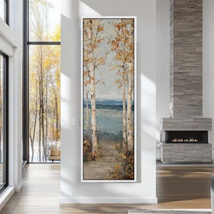 Puede incluir: Una pintura vertical enmarcada muestra un camino que conduce a un lago, flanqueado por abedules con follaje dorado. La obra de arte utiliza una paleta de colores apagados de azules, marrones y dorados, creando una escena natural y serena.