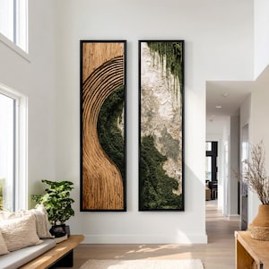 May include: Two tall, rectangular wall art pieces in black frames. The left piece features carved light wood with concentric curved lines and dark green moss. The right piece displays a textured stone-like surface with hanging green moss.