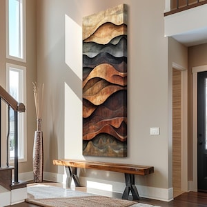 May include: A tall, rectangular wall art piece featuring layered, undulating waves of wood in varying shades of light tan, warm brown, dark espresso, and charcoal grey, creating a three-dimensional, topographical effect on the surface.