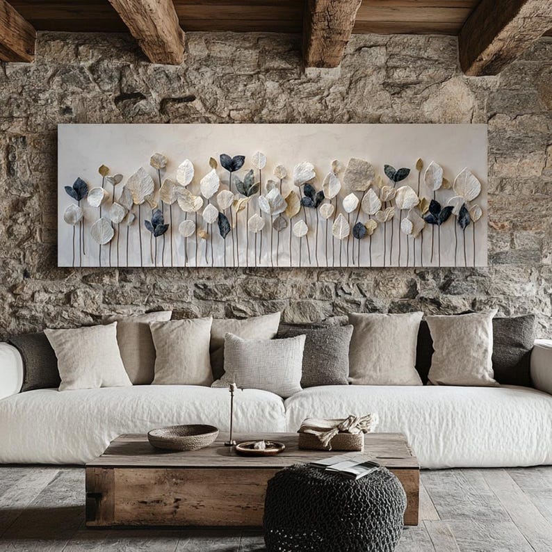 a cozy living room with a stone wall, a large white sofa, and a wooden coffee table. Above the sofa, there is a large abstract painting with white and blue leaves arranged in a repeating pattern.