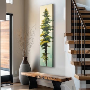 May include: A vertical painting of a tall green tree with a yellow-green crown against a light blue background. The painting is framed and hanging on a white wall in a modern home.