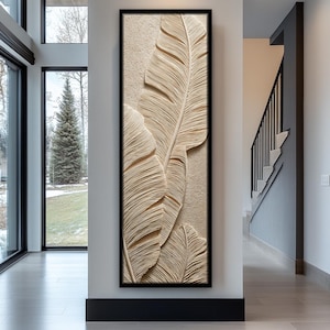 Puede incluir: Una obra de arte mural enmarcada que presenta un relieve texturizado beige de tres grandes hojas estilizadas. La obra está encerrada en un marco negro y montada en una pared de color neutro, añadiendo un toque decorativo natural.