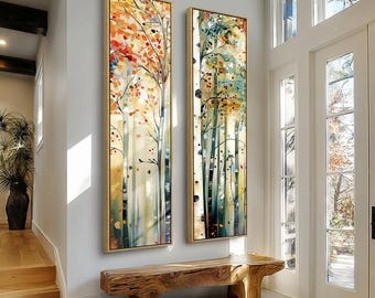 May include: Two vertical framed paintings depicting stylized trees with colorful foliage. The paintings feature a palette of orange, red, green, and yellow hues. The artwork is displayed on a white wall, with a wooden bench below.