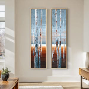 May include: A set of two vertical rectangular wall art panels featuring a forest of birch trees with white and grey bark. The background shows a soft blue sky above a horizon line, with a warm orange and brown ground covering the lower portion.
