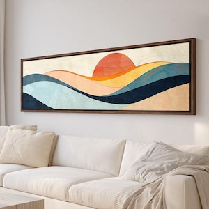 May include: A long, rectangular framed wall art piece featuring an abstract landscape with a large orange sun rising over layered, rolling hills in shades of light blue, dark blue, yellow, and cream, all set within a dark brown wooden frame.