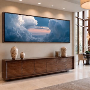May include: A panoramic rectangular wall art piece featuring a sky filled with large, voluminous white and blue clouds, with a soft pink and orange horizon line visible between the cloud formations, framed in a dark brown wooden border.