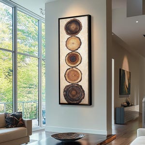 以下が含まれることがあります： モダンな抽象的なデザインの縦型の壁掛けアート作品。作品は、それぞれが独特の木目模様と色の変化を持つ、5つの円形のウッドスライスを縦に積み重ねたものです。背景は薄いベージュで、ウッドスライスは黒で額装されています。