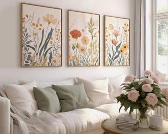 May include: Three framed floral art prints with gold frames hang above a white sofa with green cushions. The prints feature watercolour illustrations of wildflowers in yellow, orange, and green against a cream background.