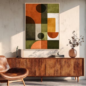 Puede incluir: Impresión artística geométrica abstracta en un marco de madera. La obra presenta un collage de formas en tonos naranja, verde, marrón y blanco. La impresión cuelga sobre un mueble de madera con una silla de cuero a la izquierda.