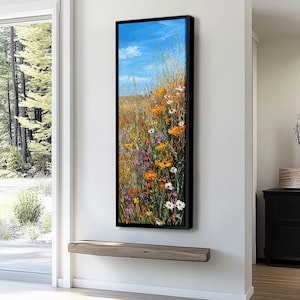 Pode incluir: Pintura vertical emoldurada de um prado de flores silvestres sob um céu azul com nuvens. A obra apresenta uma mistura vibrante de flores laranja, amarelas, roxas e brancas, com gramíneas altas. A pintura é exibida em uma parede branca.