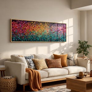 Può includere: Un grande dipinto astratto rettangolare con una cornice dorata. L'opera presenta una vibrante gamma di colori, tra cui rosso, rosa, giallo, verde e blu, creando un effetto strutturato simile a fiori. Il dipinto è appeso sopra un divano beige con cuscini decorativi.