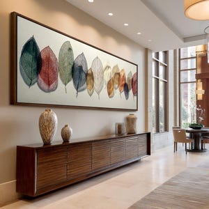 Puede incluir: Una obra de arte enmarcada, de forma rectangular, que presenta una serie de hojas coloridas. Las hojas cambian de verde a rojo, amarillo y marrón. Debajo, un mueble largo de madera oscura con jarrones decorativos.