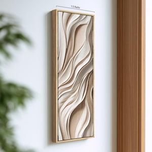 May include: A vertical rectangular wall art piece featuring a 1:3 ratio, framed in light wood. The artwork displays layered, flowing, wave-like abstract shapes in shades of cream, beige, and soft tan, creating a textured, three-dimensional effect.