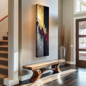 Könnte beinhalten: Vertikales abstraktes Kunstwerk mit Gold-, Schwarz-, Grau- und Burgundertönen. Unter dem Kunstwerk befindet sich eine Holzbank mit geschwungenen Beinen. Rechts von der Bank steht eine hohe, strukturierte Vase mit getrockneten Pflanzen. Die Szene spielt sich in einem gut beleuchteten Eingangsbereich ab.