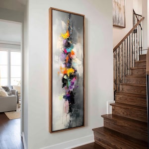 May include: A tall, rectangular framed wall art piece featuring an abstract vertical composition. The painting displays a central column of thick, textured paint strokes in vibrant yellow, orange, pink, purple, and blue against a gray background.