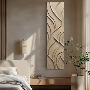 Op de afbeelding: Een verticaal, rechthoekig wandkunstwerk met een gesneden, vloeiend ontwerp. Het kunstwerk heeft een lichtbeige kleur met een textuur, golfachtig patroon. Het is gemonteerd op een neutraal getinte muur, wat een minimalistische esthetiek creëert.