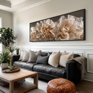 Peut inclure: Intérieur de salon avec une grande œuvre d'art abstraite encadrée en noir. L'œuvre représente un gros plan de formes douces, superposées, beiges et blanches. Un canapé en cuir noir est orné de coussins. Une table basse en bois et un pouf en cuir complètent le décor.