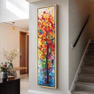 May include: A tall, vertical rectangular painting in a gold frame featuring an abstract tree with a black trunk and branches. The foliage is composed of thick, textured brushstrokes in vibrant shades of red, orange, yellow, green, and blue.